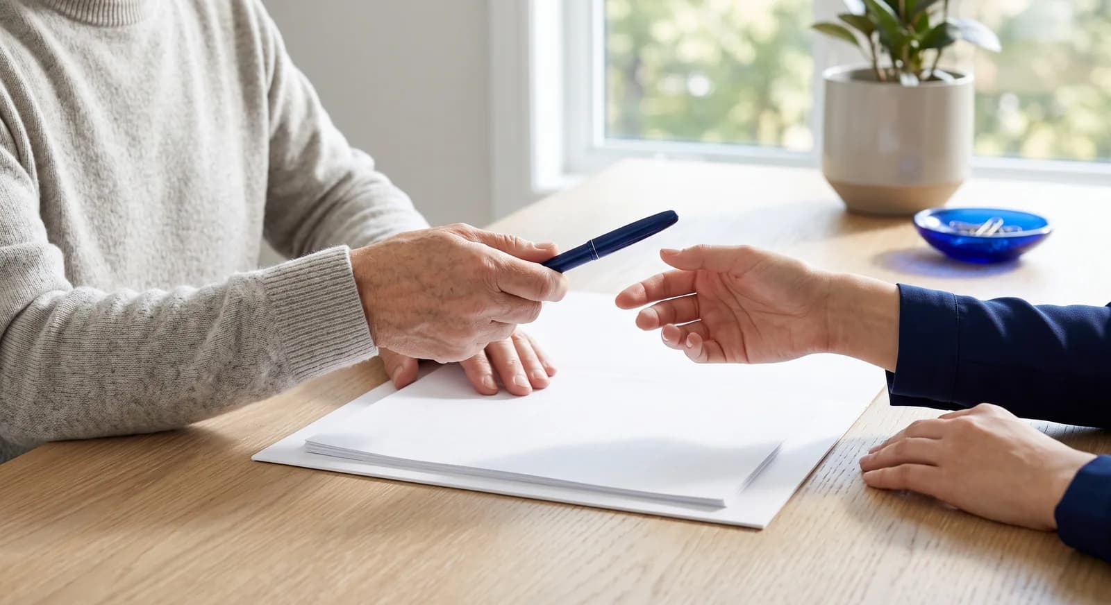 An older adult passes a pen across a document to a professional during a Will signing